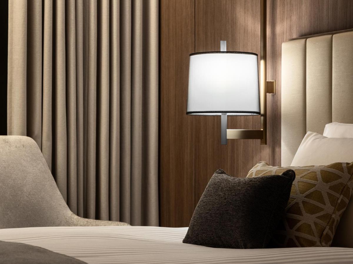 Mitsui Garden Hotel Roppongi Tokyo Premier Екстериор снимка The photo displays a cozy hotel room setting. It features a neatly made bed with white linens and several decorative pillows. To the side, there’s a stylish bedside lamp mounted on the wall with a round white shade. Behind the lamp, there are elegant