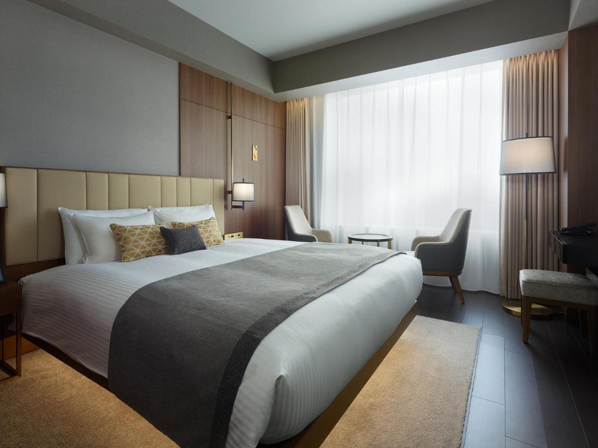 Mitsui Garden Hotel Roppongi Tokyo Premier Екстериор снимка The photo shows a modern hotel room featuring a large bed with a neatly arranged white and gray bedding. The headboard is upholstered in a light color, adding to the room's contemporary design. On either side of the bed, there are bedside lamps provi