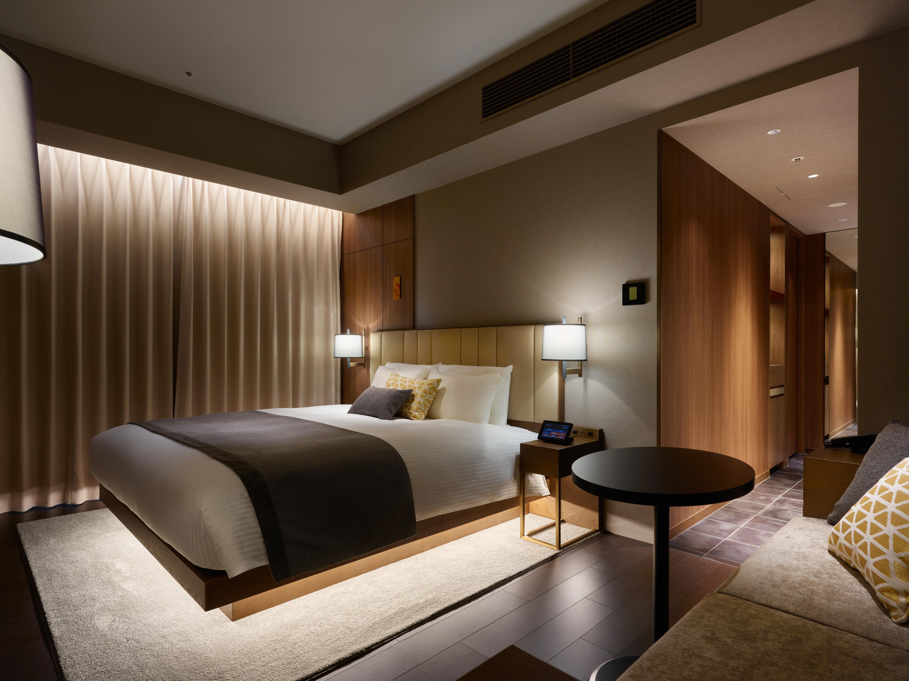Mitsui Garden Hotel Roppongi Tokyo Premier Екстериор снимка The photo shows a modern hotel room featuring a king-sized bed with neutral-colored bedding and accent pillows. There are two bedside lamps on either side of the bed, providing a warm glow. The walls have a wood finish, and there's a soft area rug on