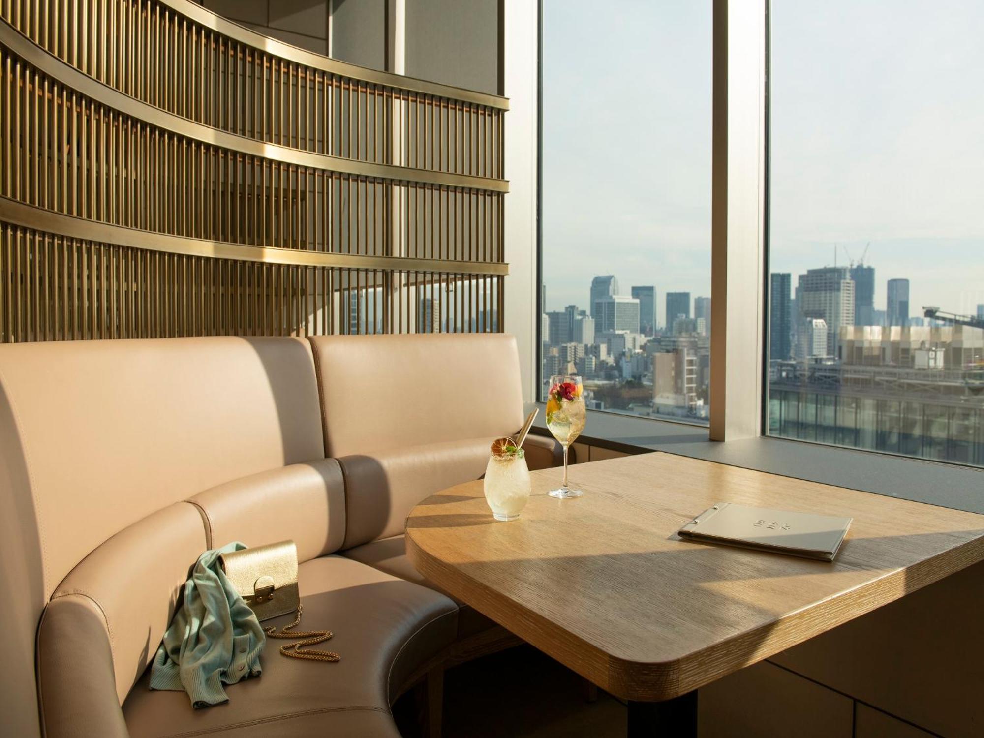 Mitsui Garden Hotel Roppongi Tokyo Premier Екстериор снимка The photo depicts a cozy, modern seating area with a curved booth that features soft, pale upholstery. A wooden table is positioned in front of the booth, and on the table, there are two elegant drinks garnished with fruit. The setting has large wind