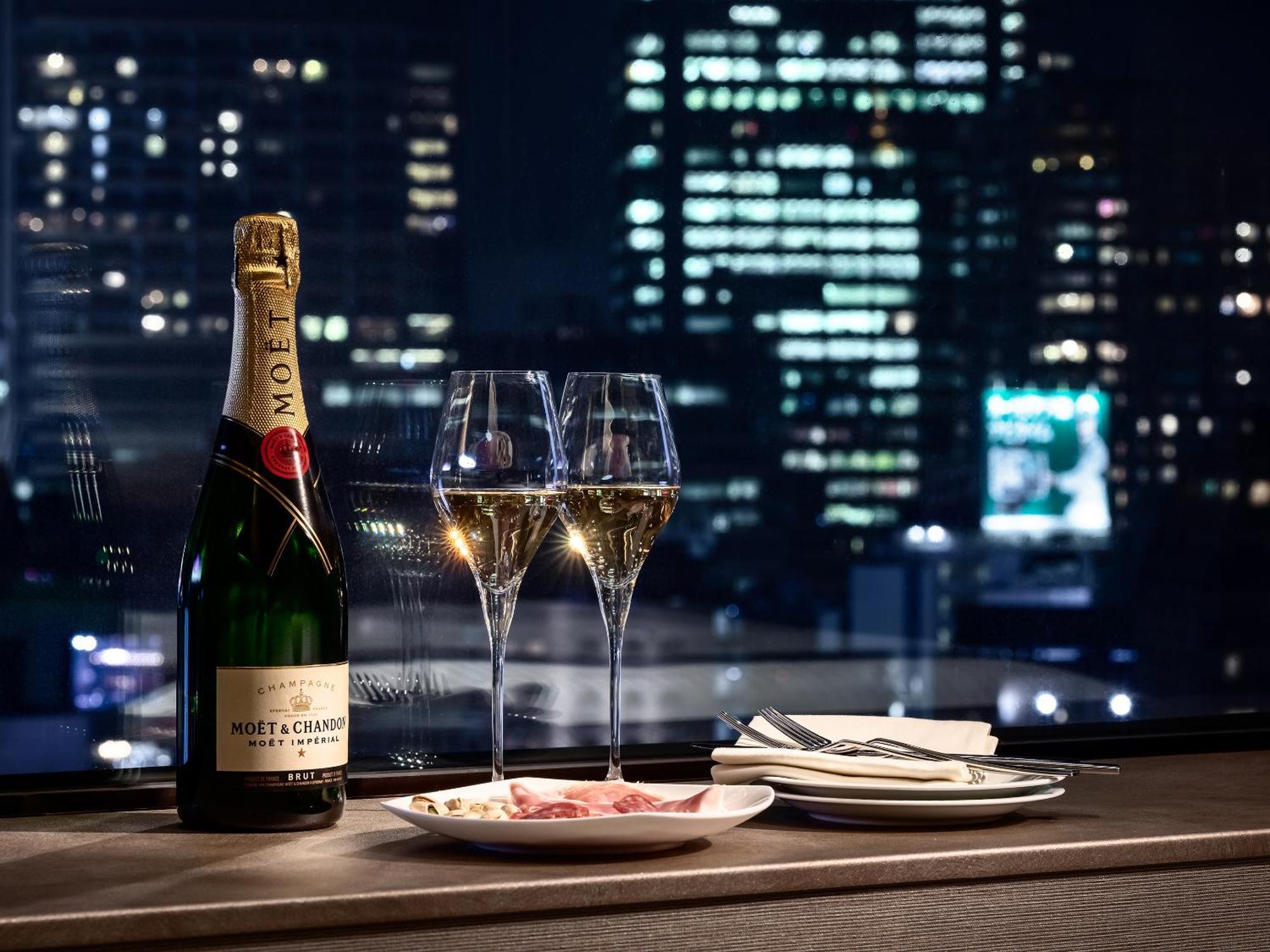 Mitsui Garden Hotel Roppongi Tokyo Premier Екстериор снимка The photo features a bottle of champagne, specifically Moët & Chandon, alongside two filled champagne glasses. The table setting includes a small plate with a selection of food and neatly arranged utensils. In the background, there is a view of a cit
