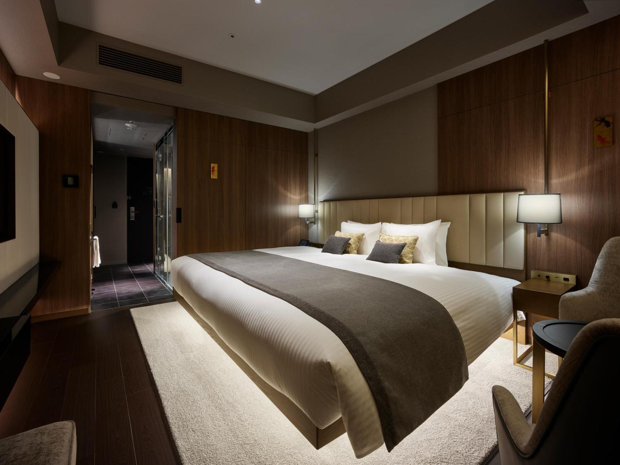 Mitsui Garden Hotel Roppongi Tokyo Premier Екстериор снимка The photo shows a modern hotel room featuring a large bed with a neutral-colored duvet and a dark throw blanket. The headboard is upholstered, and there are two bedside lamps on either side of the bed. The walls have a warm wood paneling, contributin