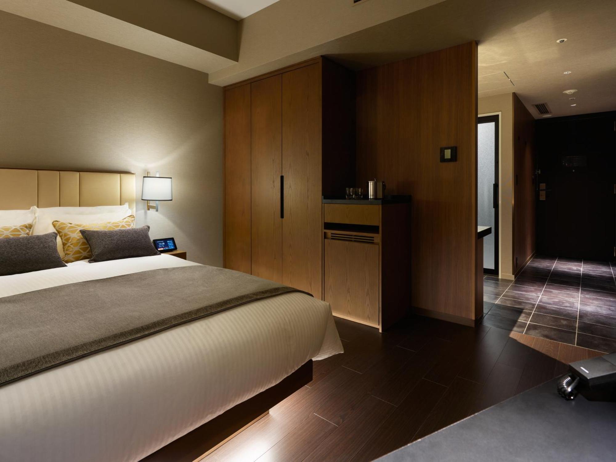 Mitsui Garden Hotel Roppongi Tokyo Premier Екстериор снимка The photo shows a modern hotel room featuring a neatly made bed with decorative pillows. The room has wooden accents, including a wardrobe and cabinetry, contributing to a warm ambiance. A bedside lamp is on one side of the bed, and there's a small a