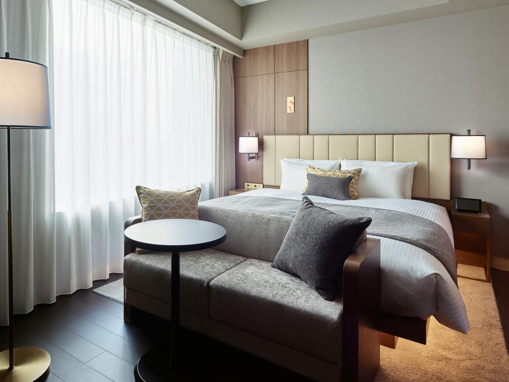 Mitsui Garden Hotel Roppongi Tokyo Premier Екстериор снимка The photo shows a modern hotel room that features a large bed with a padded headboard and soft bedding. There's a small, round table accompanied by a couch or seating area, adorned with decorative pillows. To the left, a floor lamp provides additiona